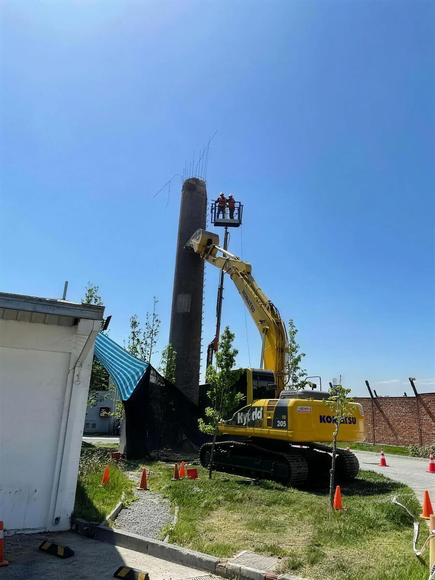 Demolición de una chimenea industrial con excavadora y alza hombre